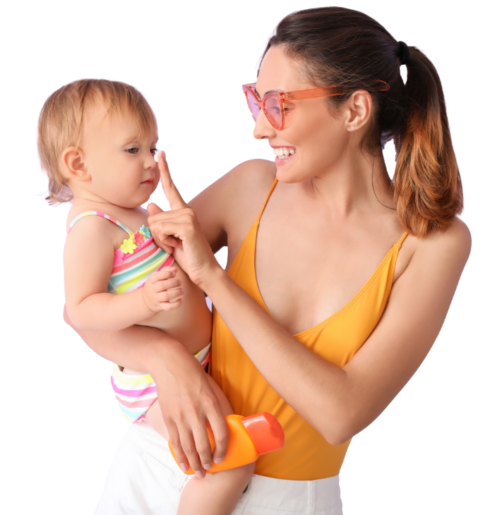 A smiling woman in an orange swimsuit playfully applies sunscreen to a baby in a striped swimsuit. She holds a sunscreen bottle