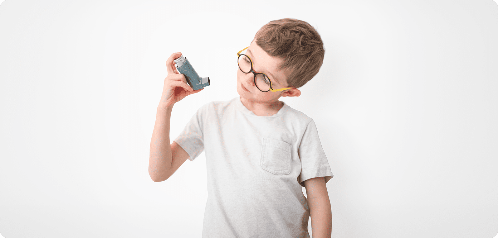 A young boy with glasses examines an inhaler against a plain white background. He wears a light-colored shirt, appearing thoughtful and curious.