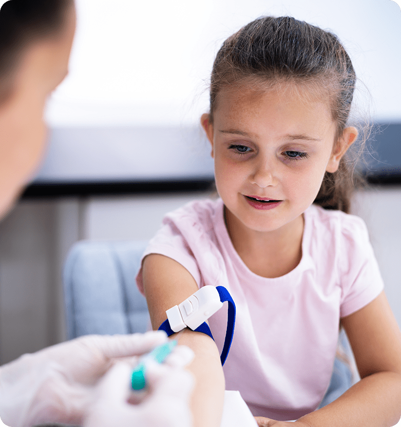A young girl with a thoughtful expression watches a healthcare professional take a blood sample. She wears a pink shirt and a blue tourniquet is on her arm.