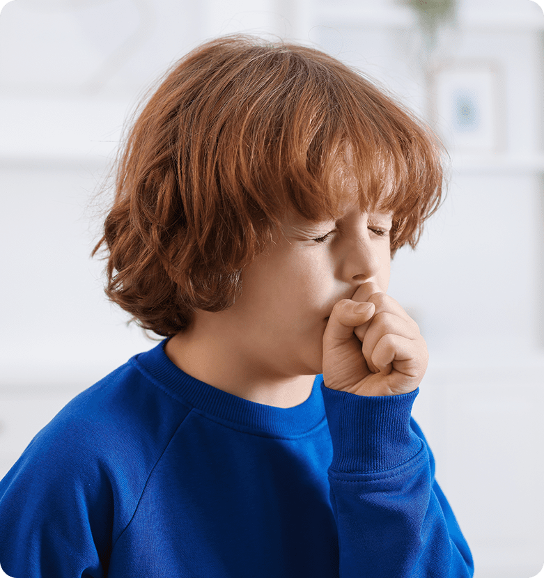 Young child with brown hair in a blue sweater coughs into their hand. They appear to be indoors, conveying a sense of discomfort or illness.