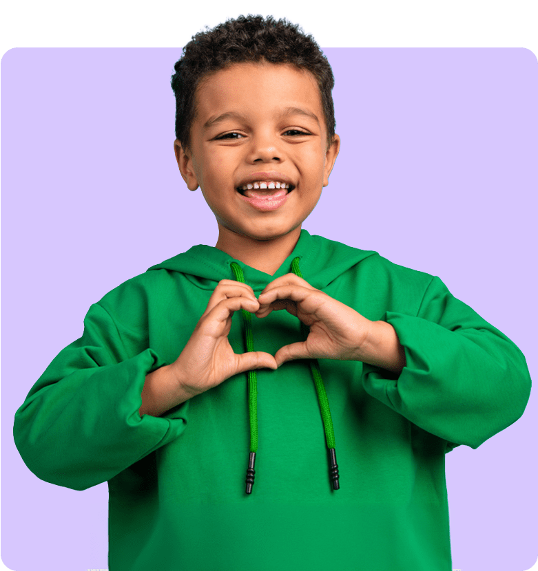 A happy child in a green hoodie makes a heart shape with hands against a purple background, smiling widely. The mood is cheerful and playful.