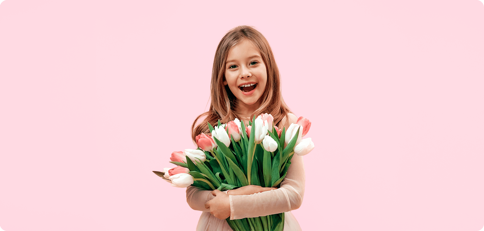 A young girl smiles brightly, holding a bouquet of pink and white tulips against a soft pink background, conveying joy and innocence.